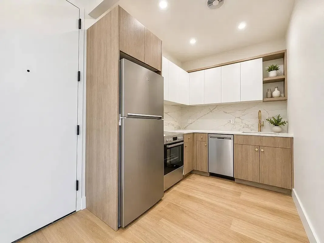 Kitchen with wood and white cabinetry, stainless steel appliances, marble backsplash, and hardwood flooring.