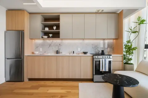 Modern kitchen with wood and beige cabinetry, stainless steel appliances, marble backsplash, and hardwood floors.