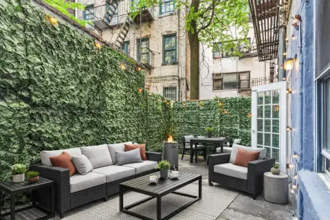 Outdoor patio with ivy-covered walls, black wicker seating, cushions, coffee table and surrounding buildings.