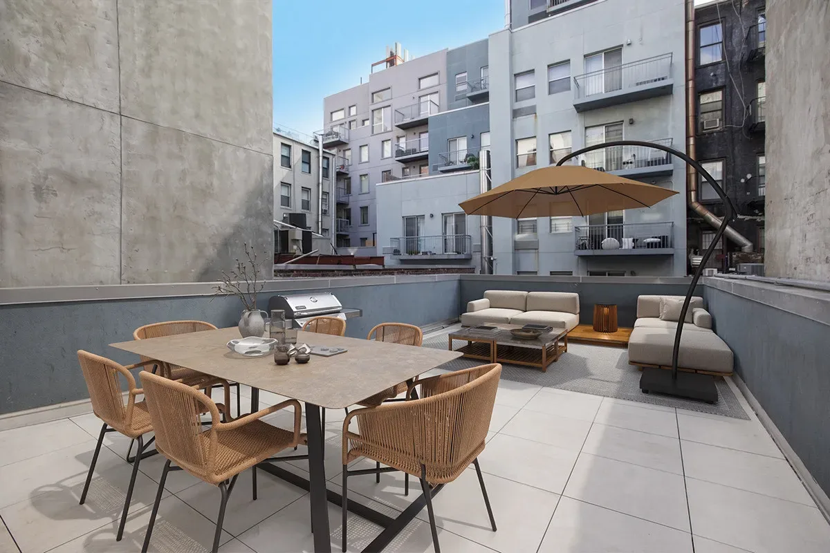 Rooftop terrace with dining table, woven chairs, umbrella, lounge seating and city views.