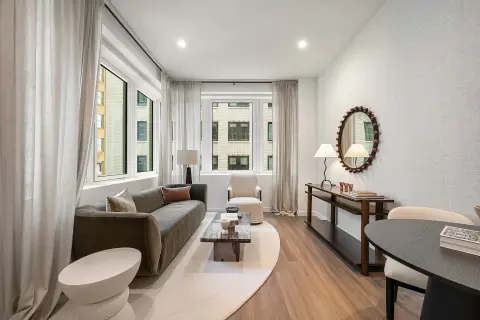 Living room with gray sofa, wooden floors, large windows with curtains, decorative mirror, and dining table.