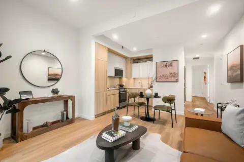 Open-plan living area with wooden floors, kitchen with light wood cabinetry, dining table, round mirror, and modern furnishings.