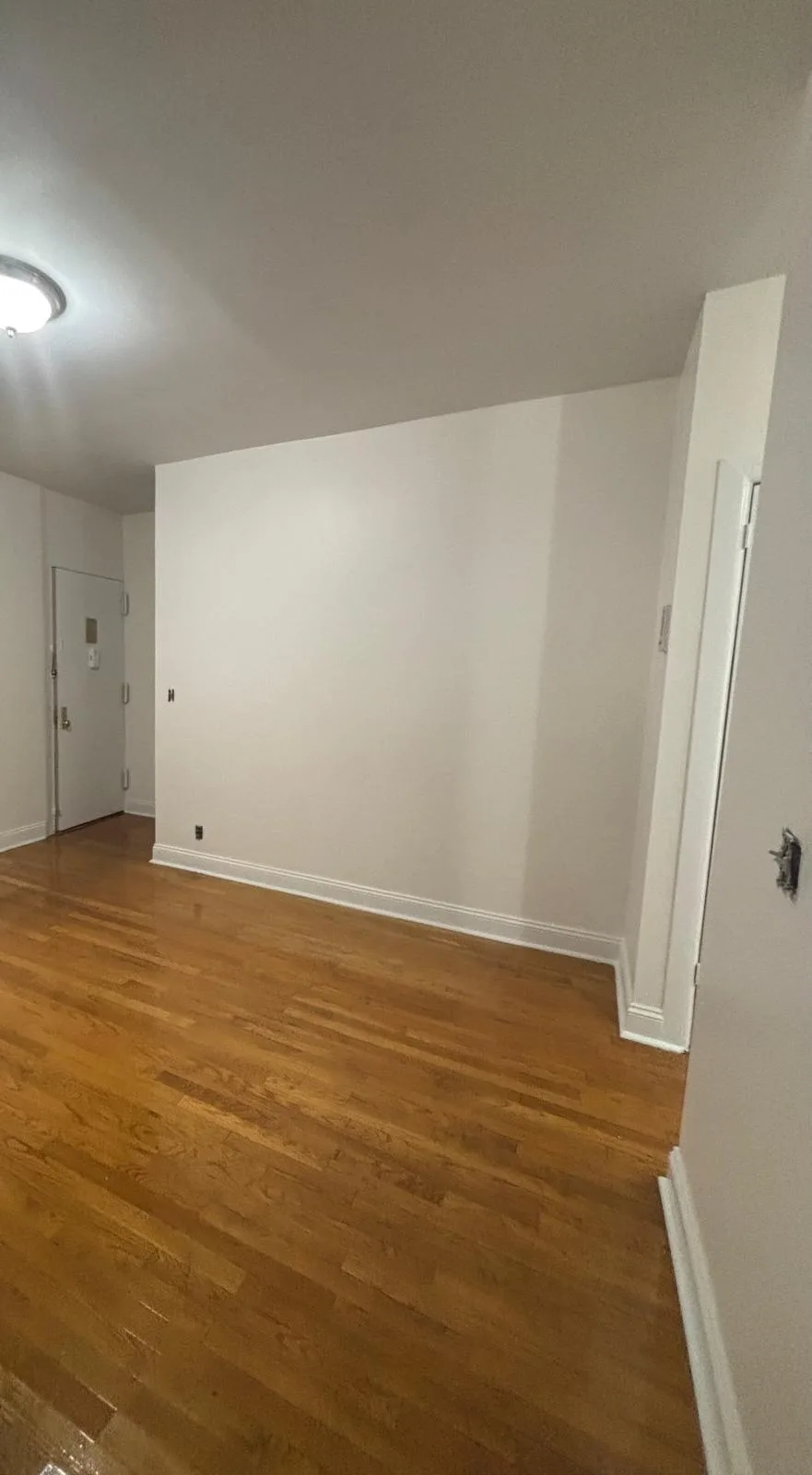 Empty room with hardwood floors, white walls, and a doorway on the right side.