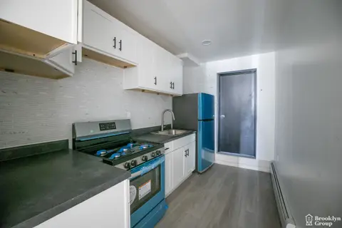 Kitchen with white cabinets, blue stove and refrigerator, dark countertops, white subway tile backsplash, and gray vinyl flooring.