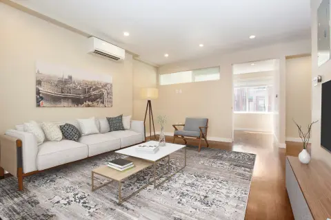 Living room with white sofa, gray armchair, patterned area rug, glass coffee table, and hardwood floors.