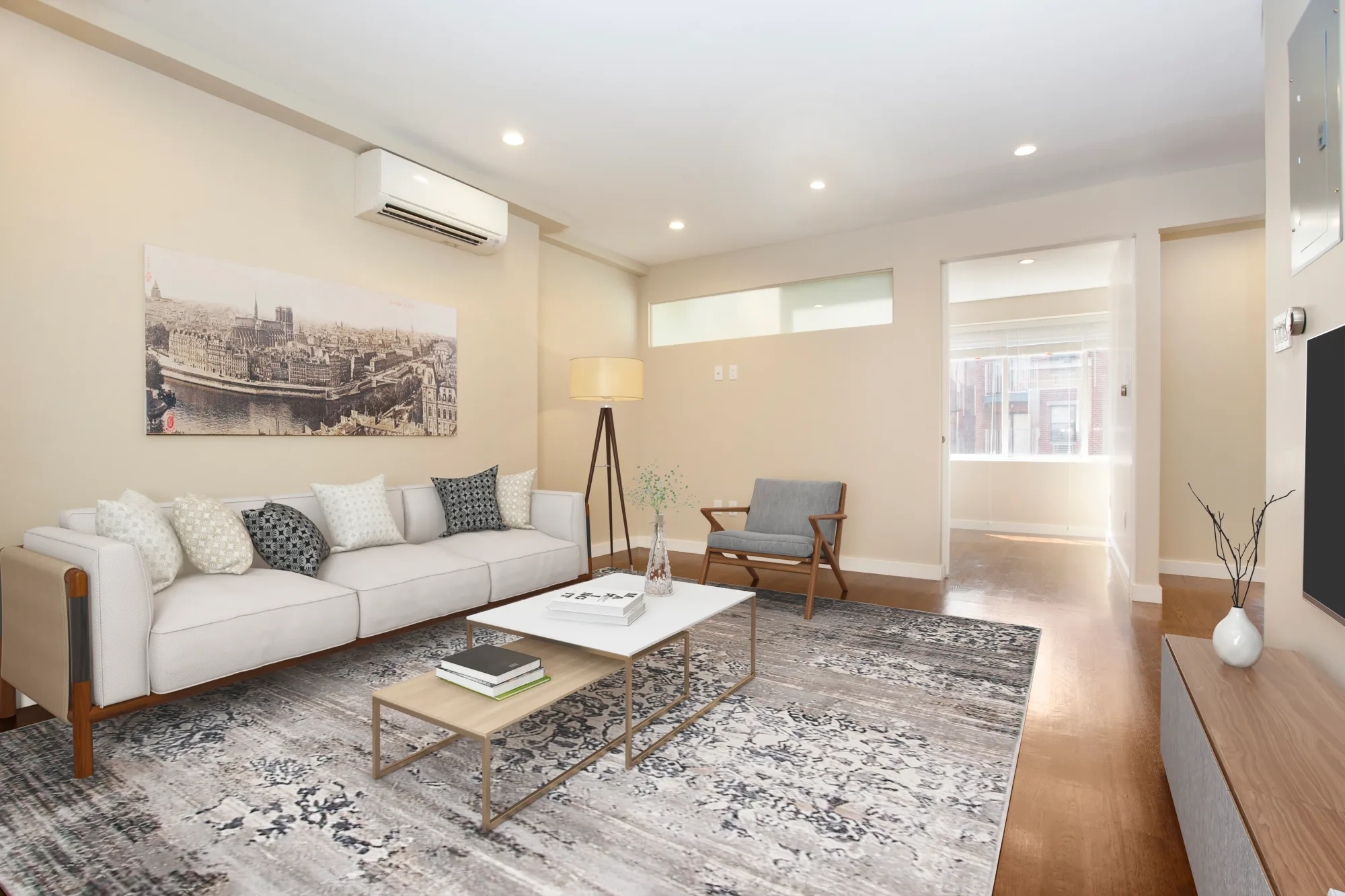 Living room with white sofa, gray armchair, patterned area rug, glass coffee table, and hardwood floors.