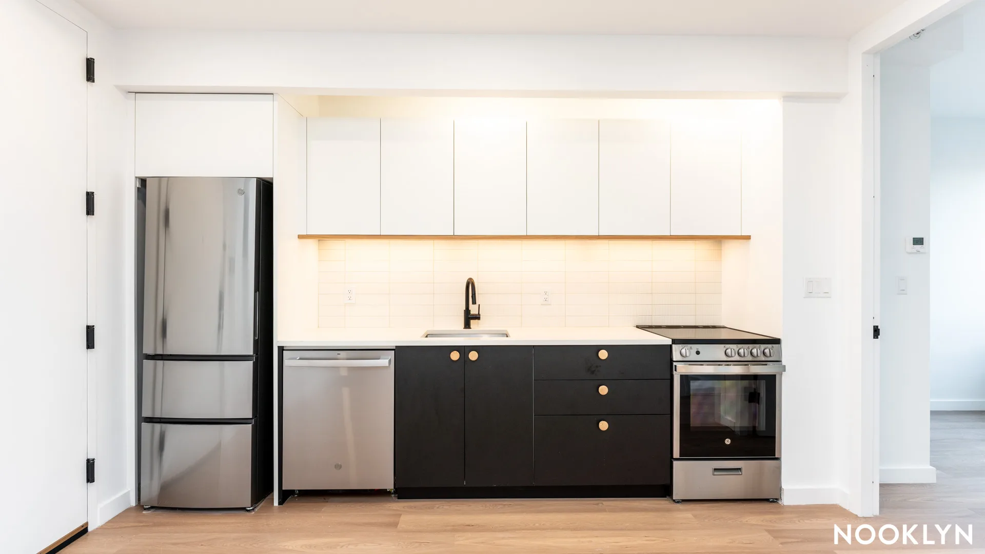 Modern kitchen with stainless steel appliances, black cabinetry, white upper cabinets, and wooden flooring.