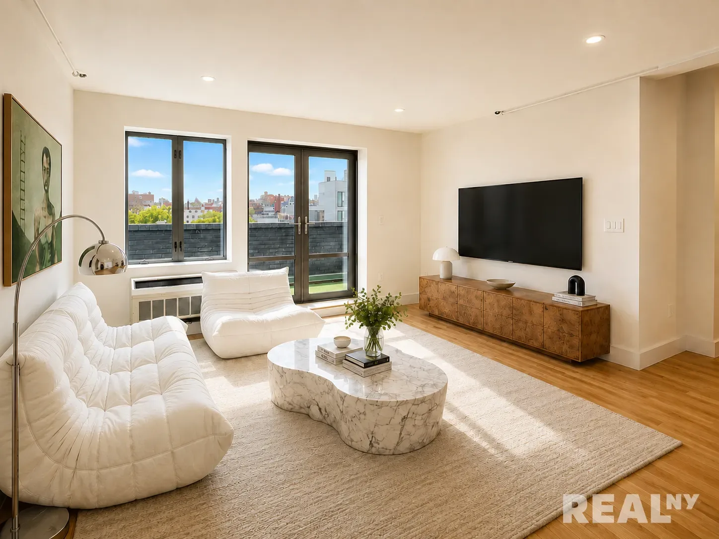 Bright living room with large windows, hardwood floors, white quilted seating, stone coffee table and wooden media console.