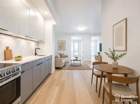 Open-plan kitchen and dining area with white cabinetry, marble backsplash, wooden dining table, and light wood flooring throughout.