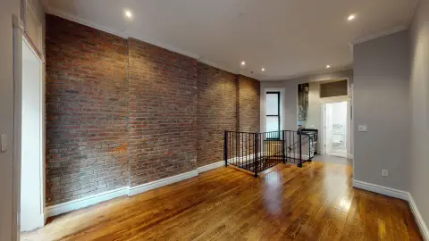 Open loft space with exposed brick wall, hardwood floors, metal railing, and recessed ceiling lights.