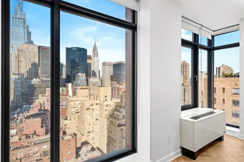 Corner room with floor-to-ceiling windows overlooking a city skyline, white walls, and hardwood flooring.