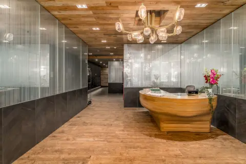 Modern lobby with wooden ceiling, pendant lights, wooden curved reception desk, and frosted glass partitions.