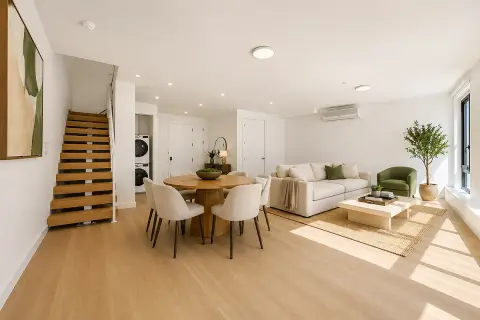 Open-plan living space with wooden dining table, cream chairs, light wood flooring, sofa, and staircase to upper level.