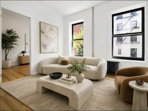 Modern living room with curved beige sofa, cream ottoman, wooden floors, large windows, and contemporary furnishings.