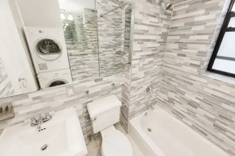 Bathroom with gray and white striped tile walls, white toilet, sink, bathtub, and glass shower enclosure.