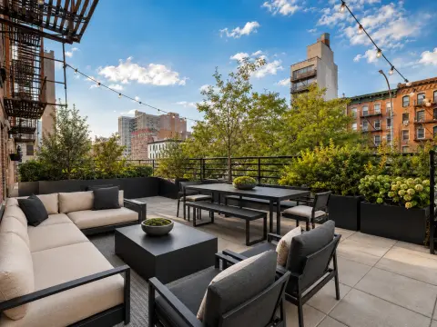 Rooftop terrace with seating areas, dining table, potted plants and city skyline views.