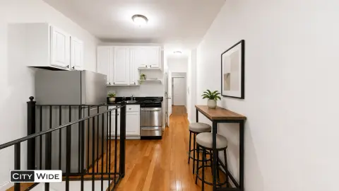 Kitchen with white cabinets, stainless steel appliances, hardwood floors, and a small dining area with bar seating.