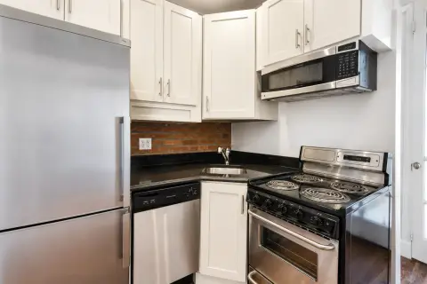 Kitchen with white cabinets, stainless steel appliances, black countertops, and a microwave above the stove.