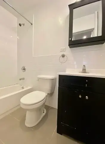 Bathroom with white subway tile walls, black vanity with sink, framed mirror, toilet, and bathtub with shower enclosure.