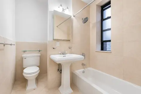 Bathroom with pedestal sink, toilet, bathtub, mirror cabinet, and window with natural light.