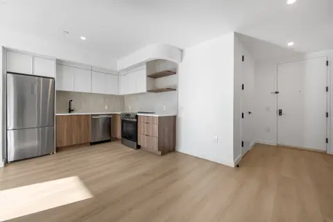 Open-concept kitchen and living area with white cabinetry, stainless steel appliances, wood flooring, and recessed lighting.