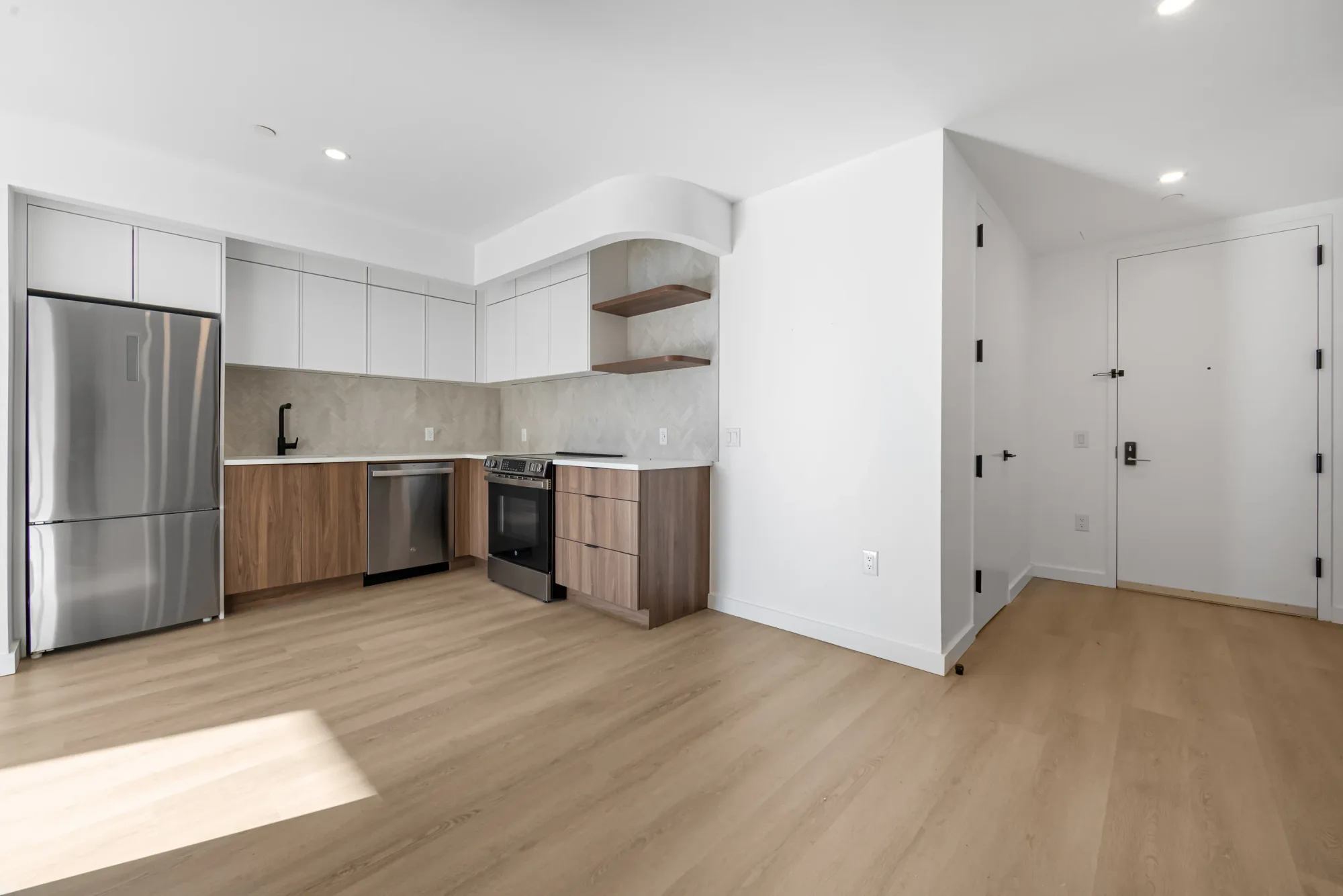 Open-concept kitchen and living area with white cabinetry, stainless steel appliances, wood flooring, and recessed lighting.