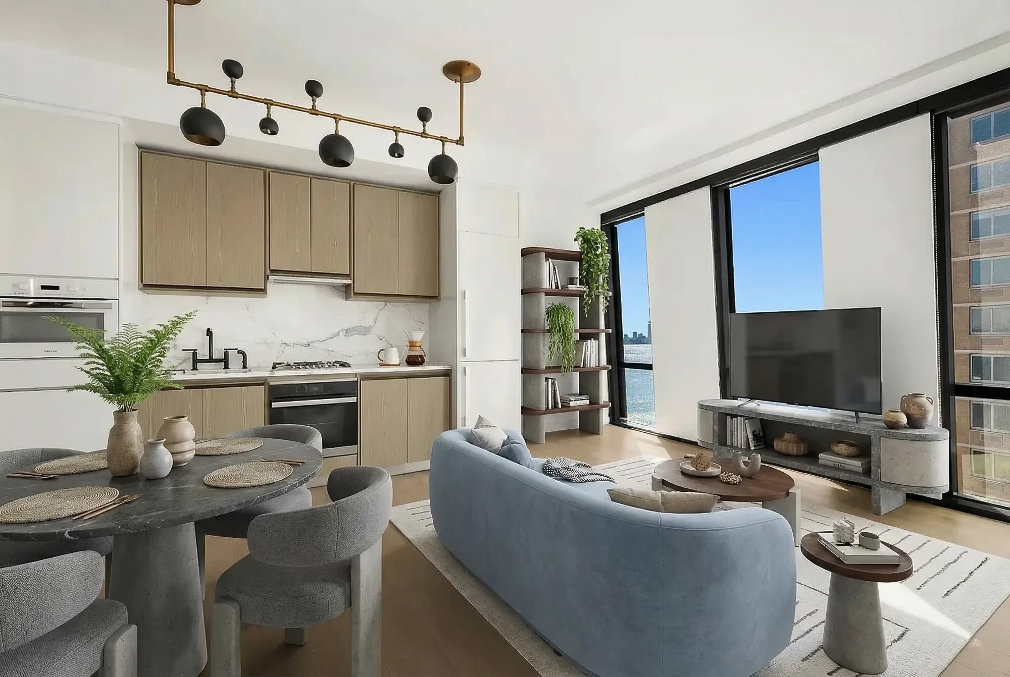 Open-plan kitchen and living room with light wood cabinetry, dining table, blue sofa, and large windows with city views.