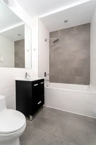 Modern bathroom with black vanity, white toilet, large mirror, and gray tile shower enclosure.