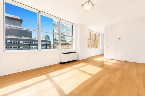 Bright living room with large windows overlooking city skyline, hardwood floors, and white walls.