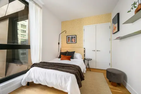Bedroom with single bed, yellow brick accent wall, white wardrobe, wooden floor, and window with white curtains.