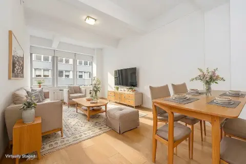 Open-plan living and dining area with wooden furniture, beige seating, dining table, TV unit, and large windows with natural light.