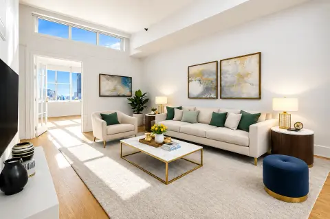 Bright living room with beige sofa, glass coffee table, hardwood floors, large windows with city views, and framed abstract artwork.