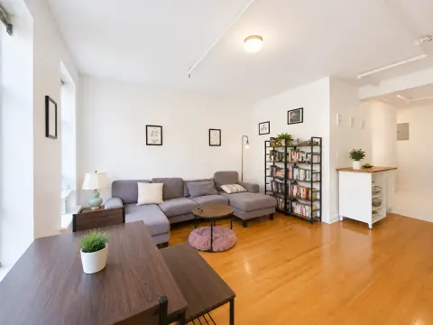 Open-plan living room with gray sectional sofa, wooden dining table, bookshelf, and hardwood floors throughout.