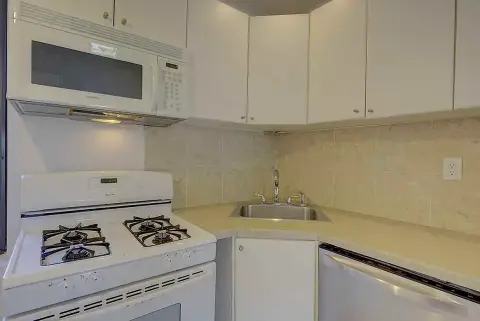 Kitchen with white cabinets, gas stove, microwave, sink, and yellow tile backsplash.