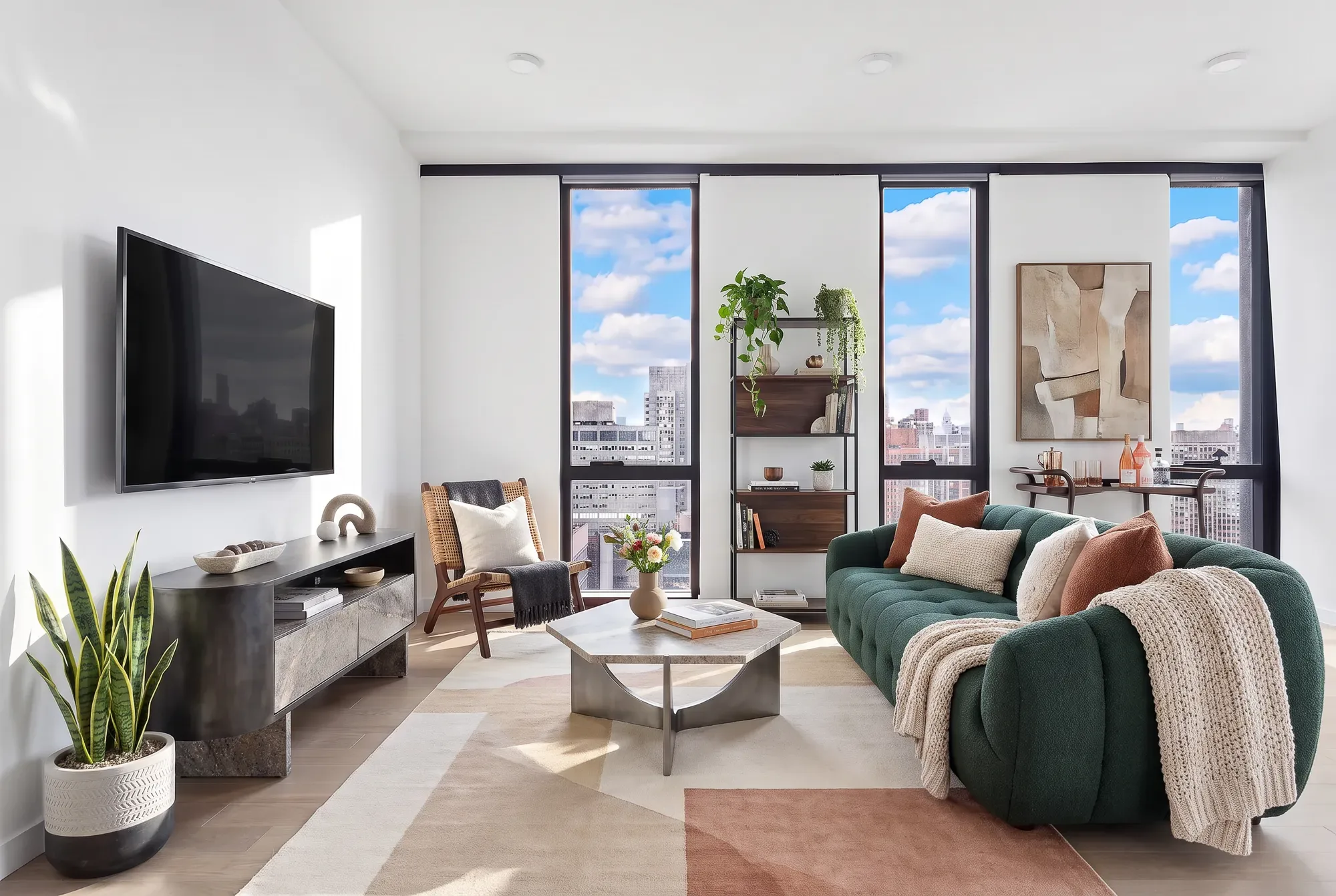 Modern living room with green sofa, wall-mounted TV, floor-to-ceiling windows overlooking city skyline, and light wood flooring.