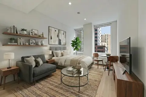 Living room with gray sofa, wooden shelving, glass coffee table, area rug, and large windows overlooking city buildings.