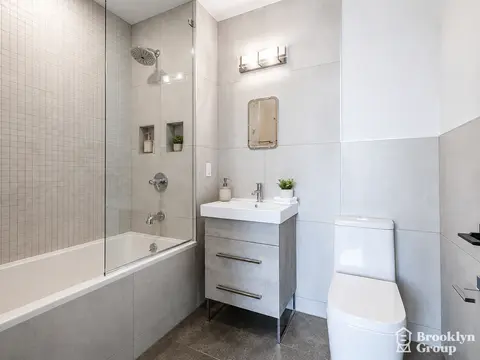 Modern bathroom with white subway tile walls, glass shower enclosure, vanity sink, toilet, and small potted plant on counter.