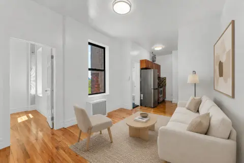 Studio apartment with hardwood floors, cream sofa, wooden coffee table, and window with natural light.
