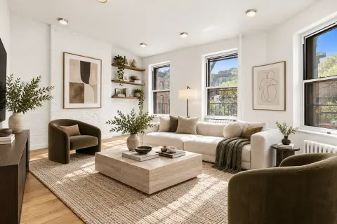 Bright living room with beige sofa, olive armchairs, wooden coffee table, large windows, hardwood floors and potted plants.