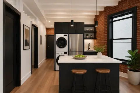 Modern kitchen with black island, stainless steel appliances, exposed brick wall, and hardwood floors.