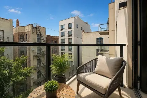 Rooftop terrace with wooden deck, black railing, armchair, potted plants, and urban building views.