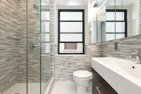 Modern bathroom with gray tile walls, glass shower enclosure, white toilet, and floating vanity with white sink.