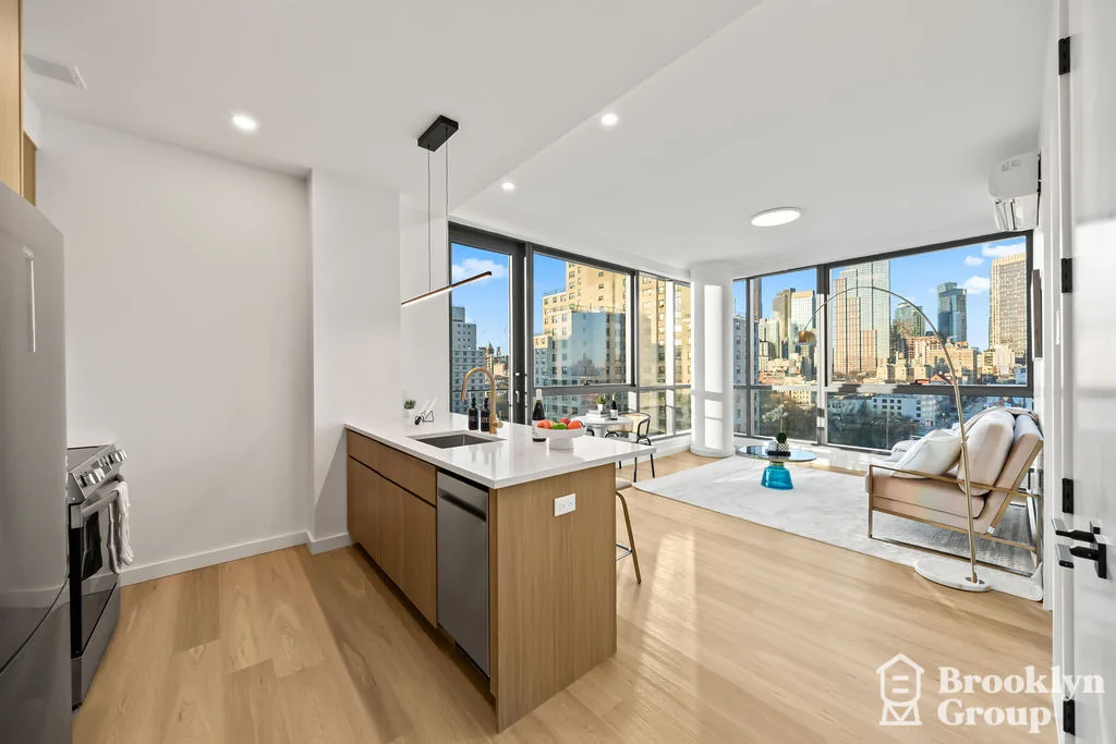 Modern kitchen and living area with wood flooring, island counter, large windows overlooking city skyline, and contemporary furnishings.