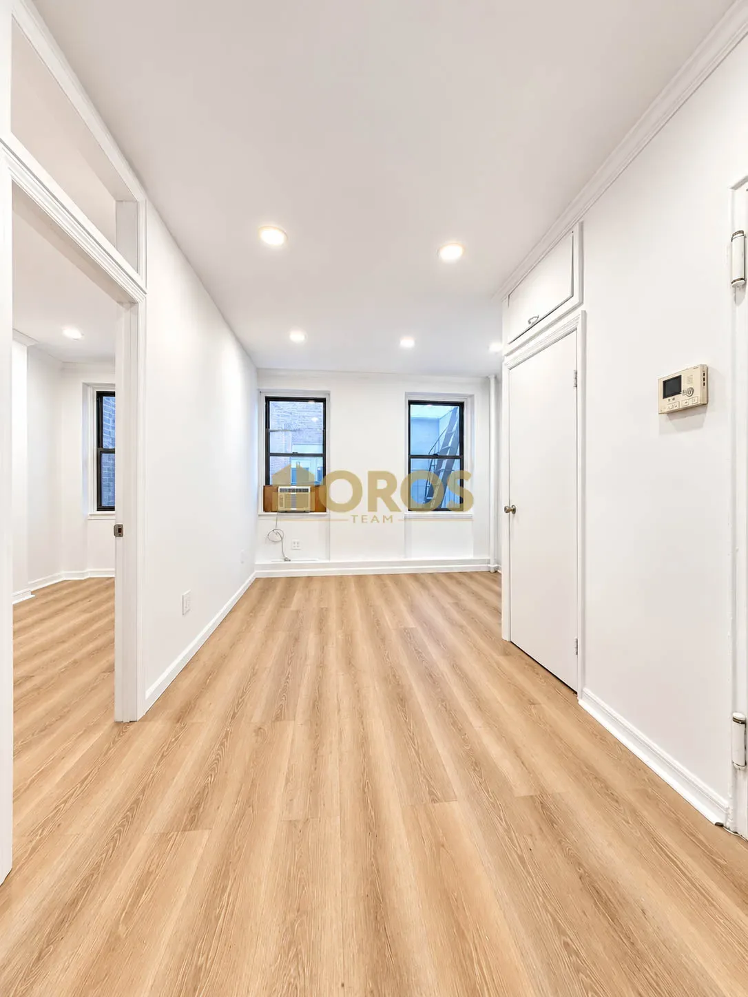 Bright hallway with light wood flooring, white walls, recessed ceiling lights, and multiple doors leading to other rooms.