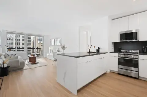 Open-concept kitchen and living room with white cabinetry, stainless steel appliances, island counter, hardwood floors and large windows.
