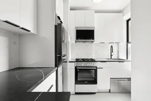 Modern kitchen with white cabinetry, black marble countertop, stainless steel appliances and built-in microwave.