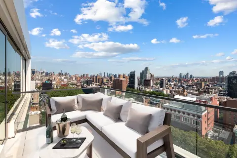 High-rise balcony with L-shaped sectional sofa, city skyline views, and floor-to-ceiling windows.