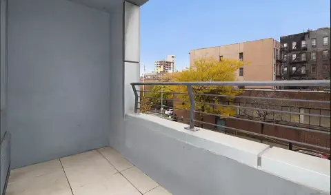 Balcony with tile flooring, metal railing, and view of surrounding buildings and trees.