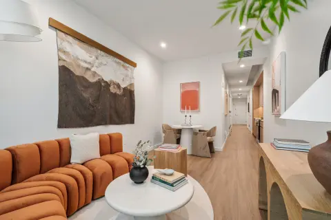 Living room with orange curved sofa, white round table, wooden flooring, and artwork on walls.