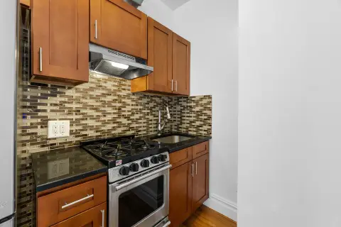 Kitchen with wood cabinets, black granite countertop, stainless steel gas range, and mosaic tile backsplash.